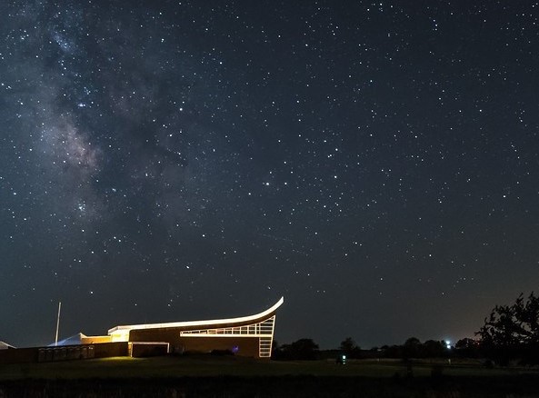 A lit building stands underneath a starry night sky. A lit building stands underneath a starry night sky.