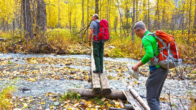 Two people crossing a creek on wood polanks.