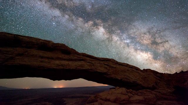 A natural arch formation frames this view of the Milky Way and constellations at Canyonlands NP
