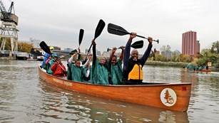 Many people in a canoe on river with paddles in the air.