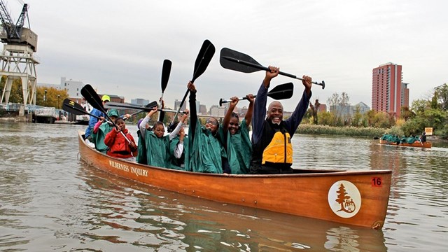 Many people in a canoe on river with paddles in the air.