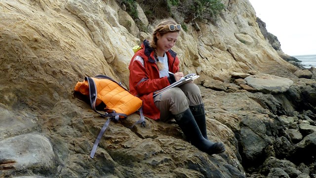 photo of a person sitting on a coastal bluff and writing in a notebook