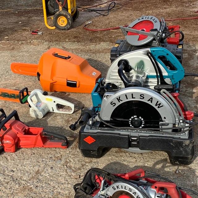 Various power tools, including circular saws and chain saws, on a wooden floor.