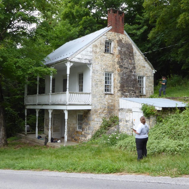 Two story historic home built into a hill side. A person in uniform stands nearby.