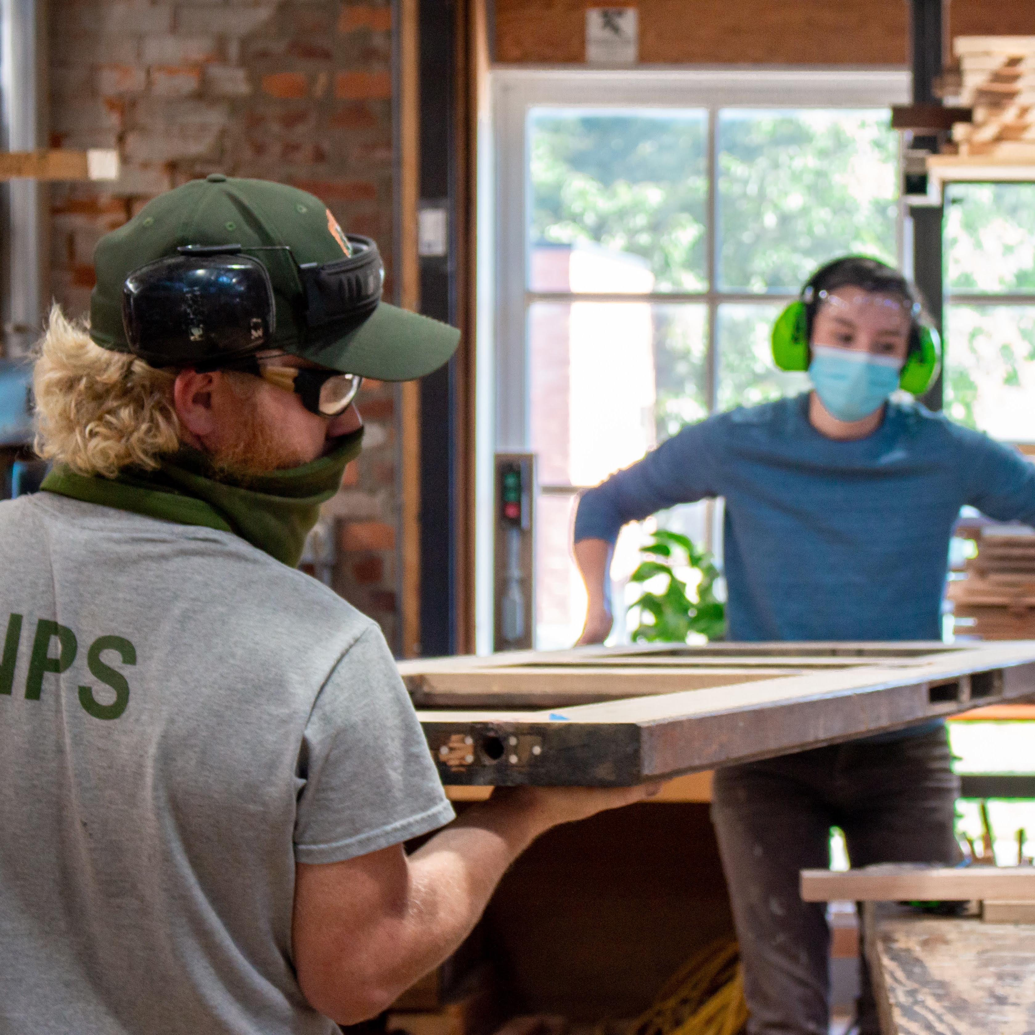 Two workers carry a large door. One worker has an NPS uniform on.