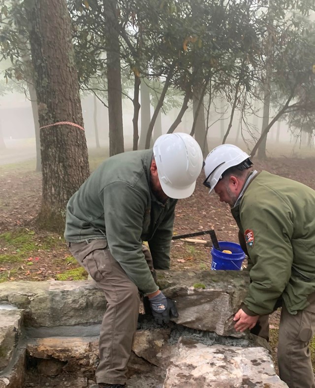 Two people in hard hats and NPS uniforms work on a large log.