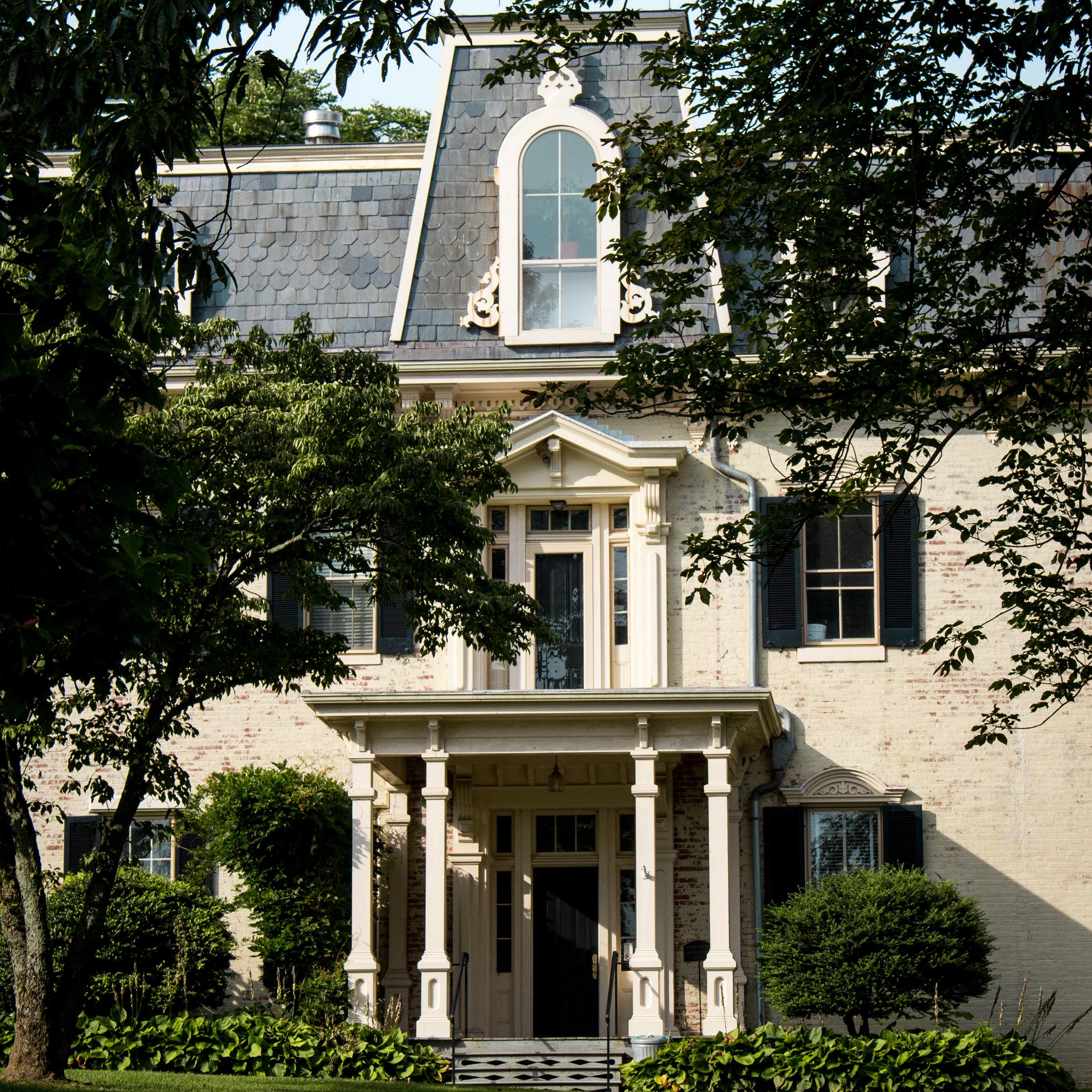 Historic three-story tall home with large trees in front.