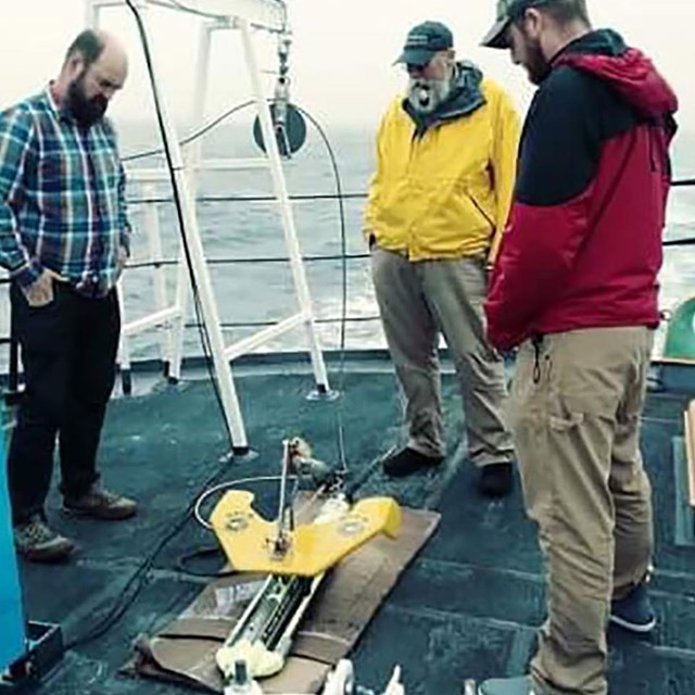 Archeologists onboard ship examine instrument platform.