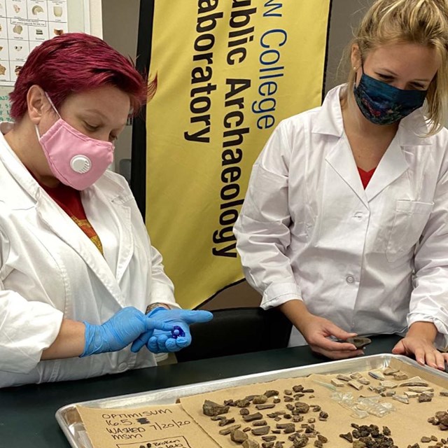 Two female-presenting people review archaeological discoveries in a laboratory.
