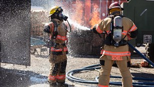 A firefighter uses a hose to spray off another firefighter.