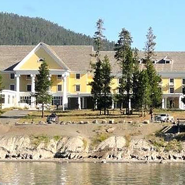 Photograph taken from the water of a large yellow hotel along a lake coastline