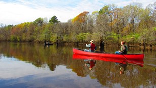 Two park visitors paddle a red canoe on a small lake