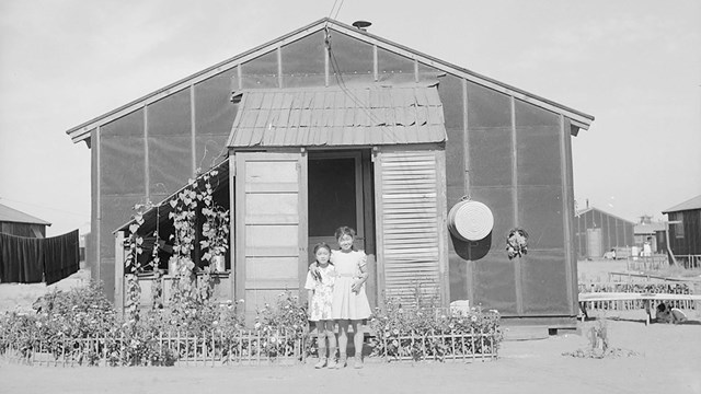 historic image of two children standing in front of barracks and flower garden.