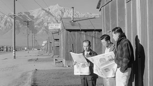 Roy Takeno (Editor) and group reading Manzanar paper in front of office. (Ansel Adams)