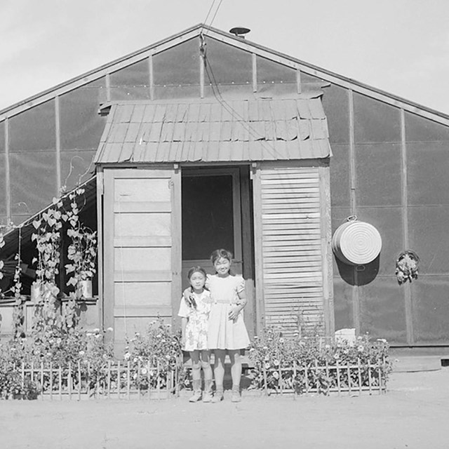historic image of two children standing in front of barracks and flower garden.