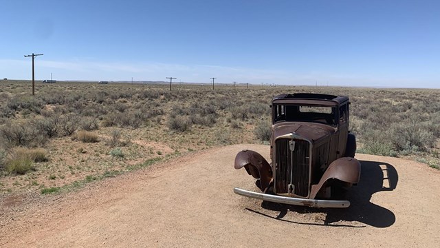 A historic rusted car sits in the desert.