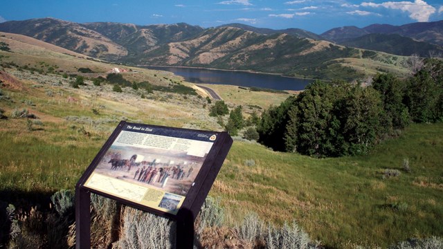 A picture of an exhibit sign on an overlook of an expansive mountain view.