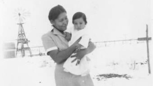 A woman holds a young child in a historical photo from the 20th century.