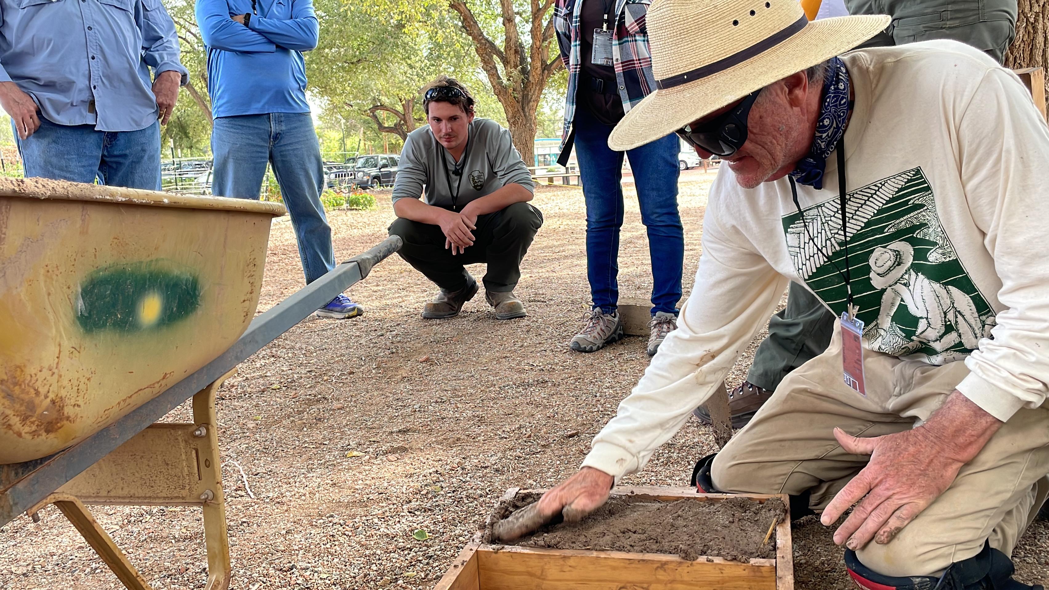 Man filling an adobe brick mold with several people watching.