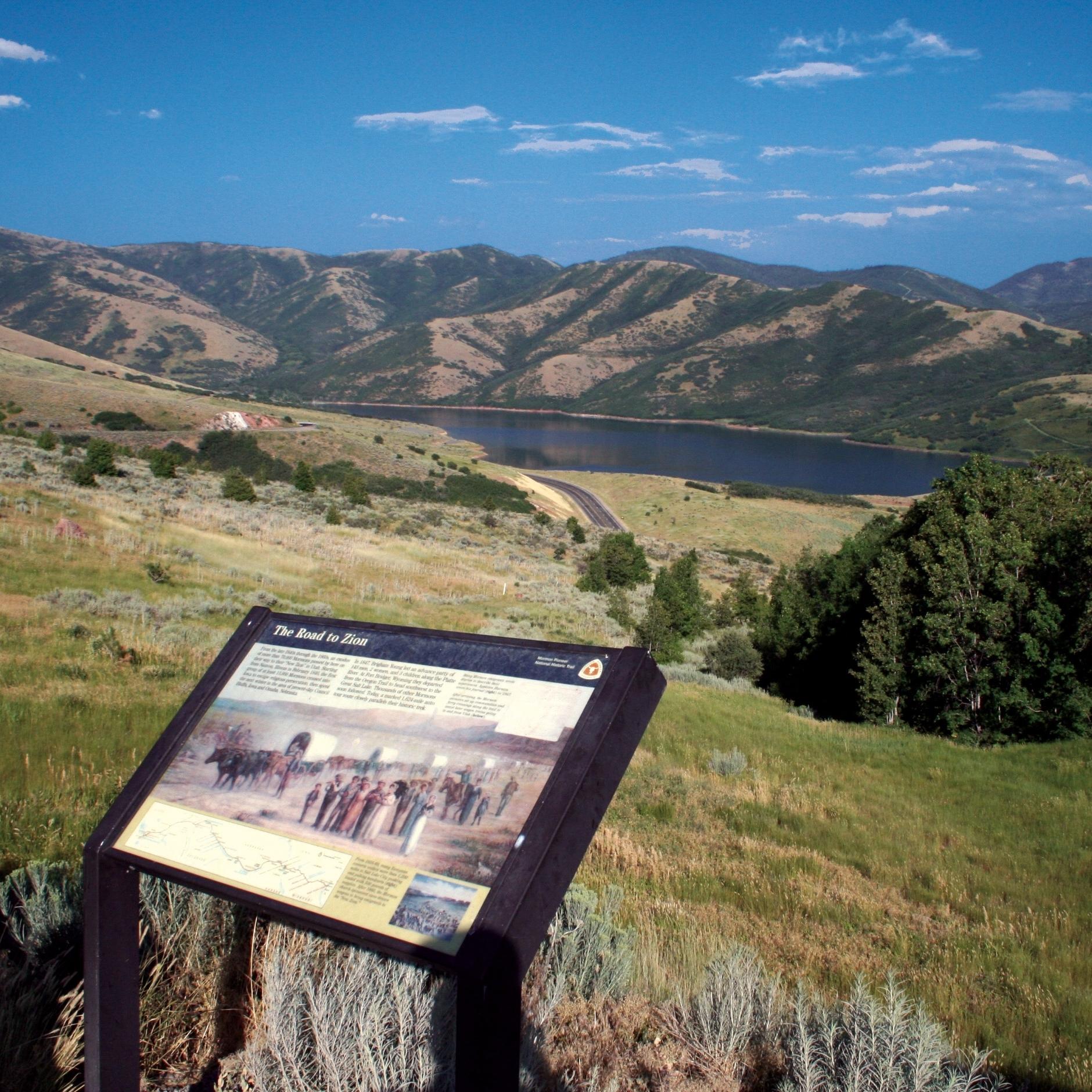 A picture of an exhibit sign on an overlook of an expansive mountain view.