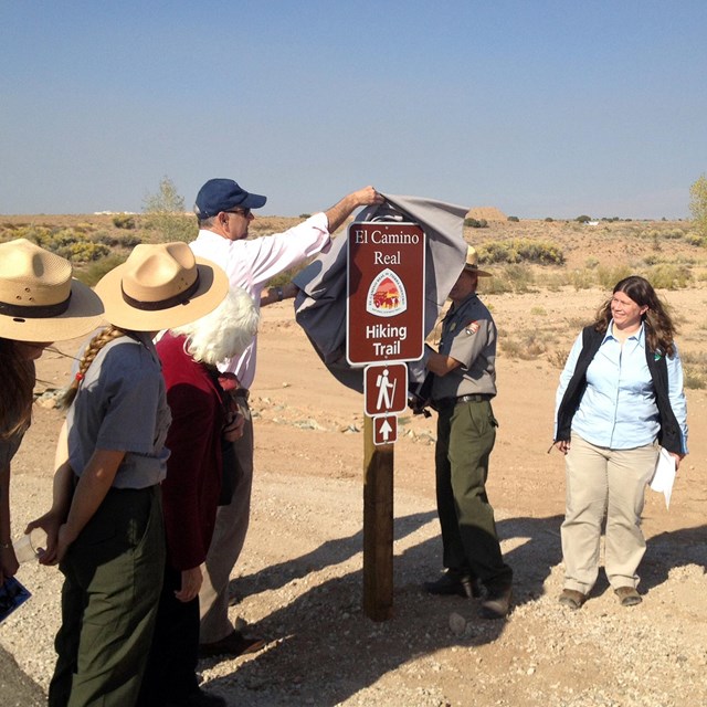 people outside standing on a road unveiling a trail sign, one black dog on leash