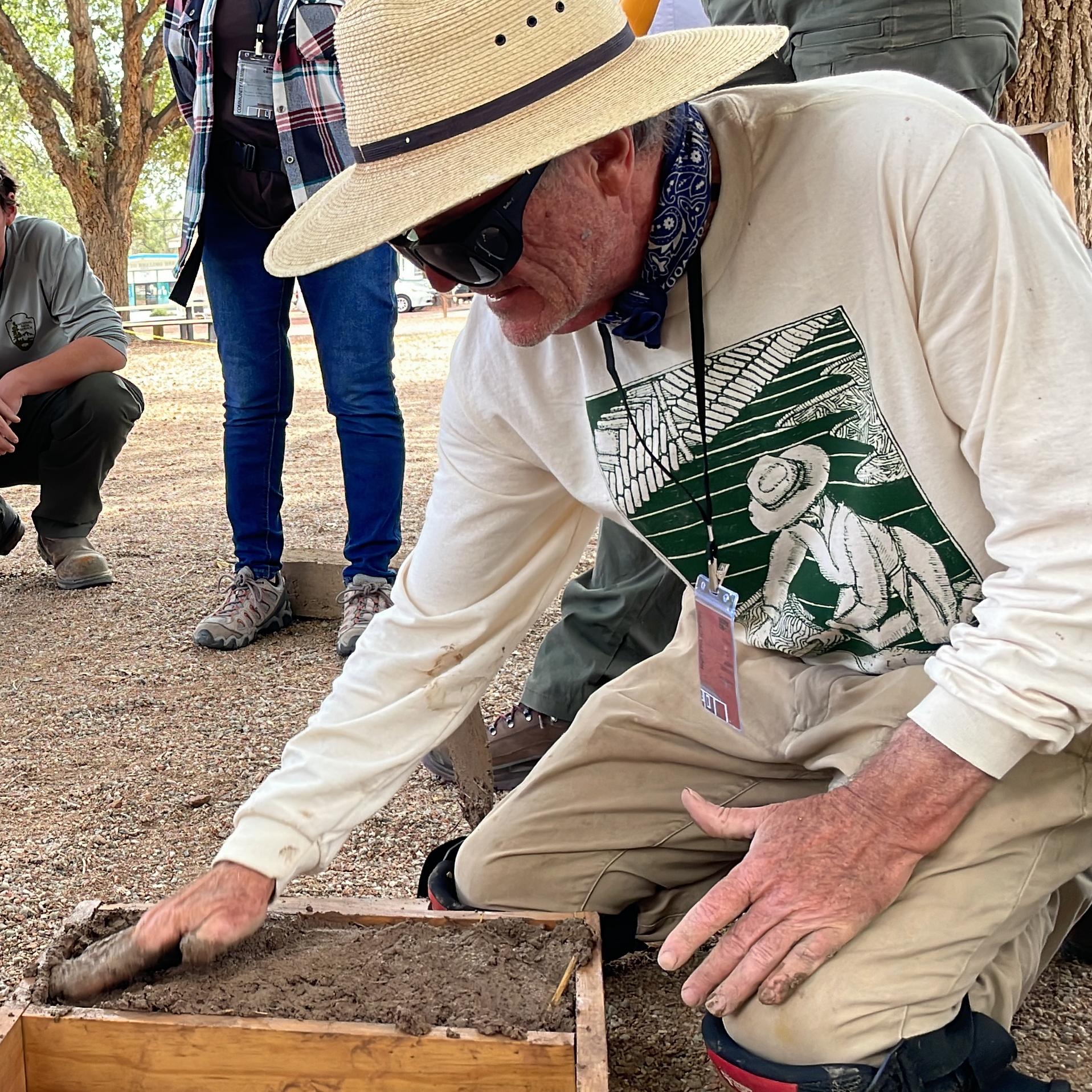 Man filling an adobe brick mold with several people watching.