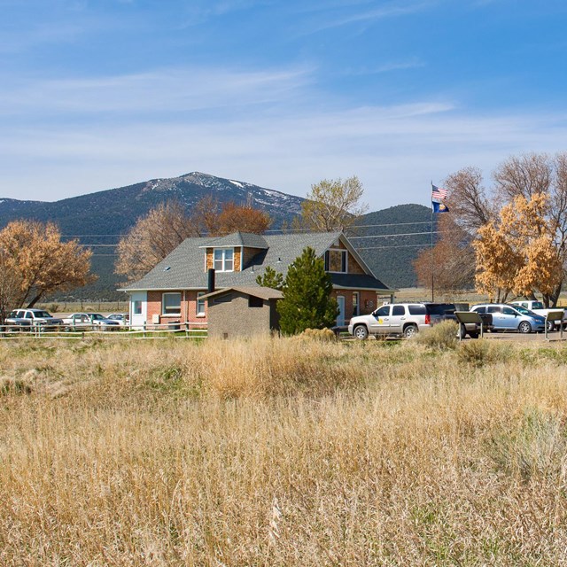 Red brick visitor center building with dark shingled roof surrounded by small trees and grass