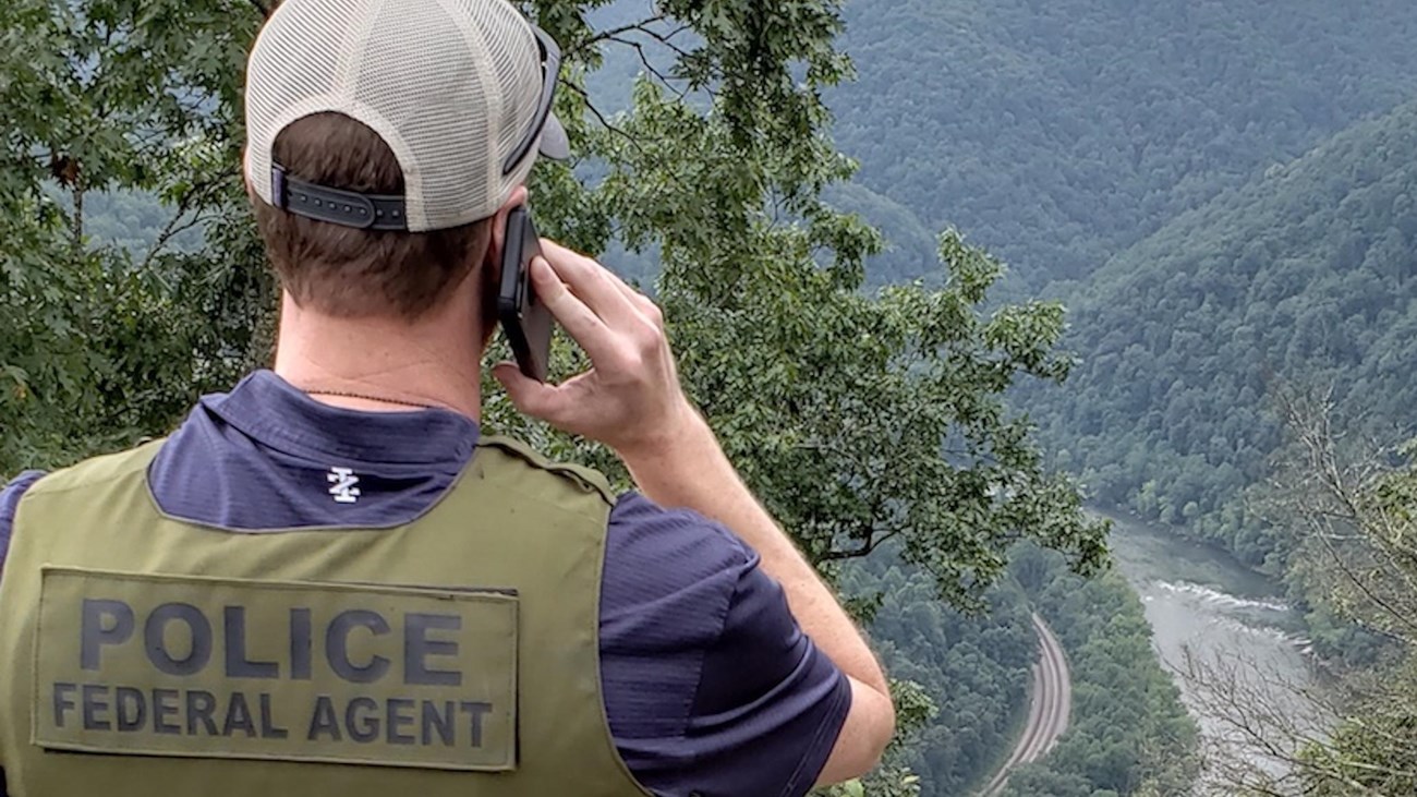 A special agent of the NPS Investigative Services Branch stands at a forested overlook above a river