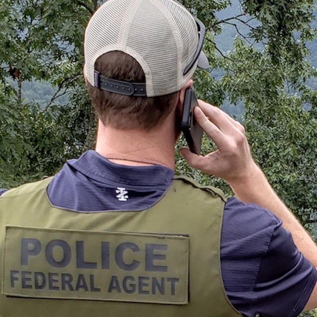 A special agent of the NPS Investigative Services Branch stands at a forested overlook above a river