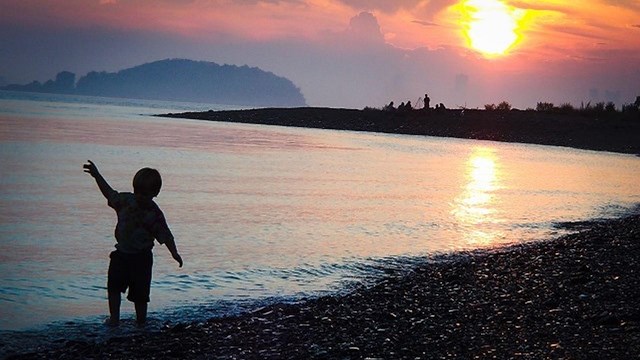 A boy dances on the beach with a sunset in the background.