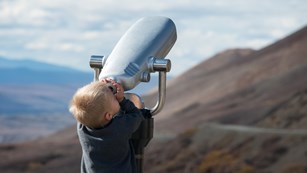 Small boy looking through binoculars into the sky. NPS/Lian Law