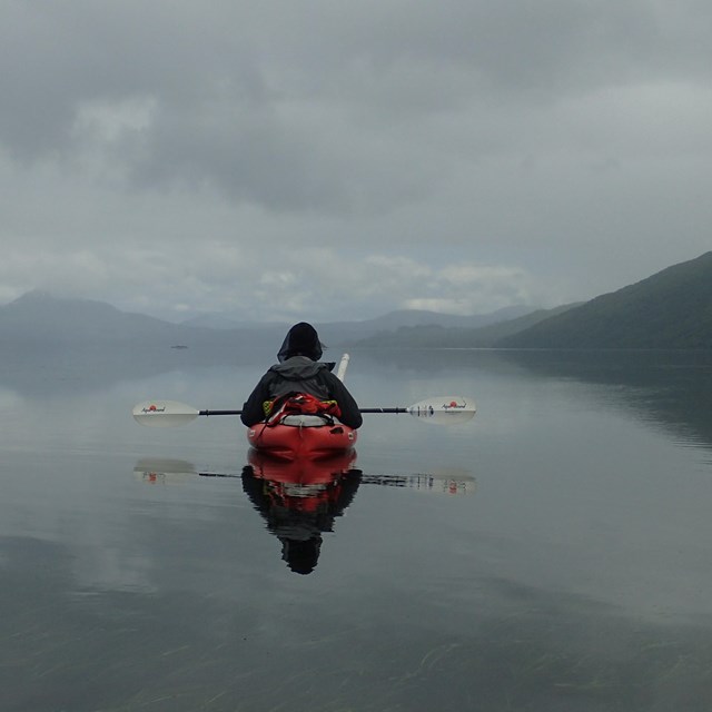 solitary kayaker on grey, still water with fog in distance