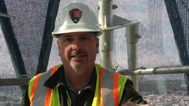 NPS Engineer stands with hardhat and work vest on at a job site.