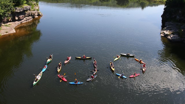 Fly over view of kayaks on the river in the shape of the numbers 1-0-0. 