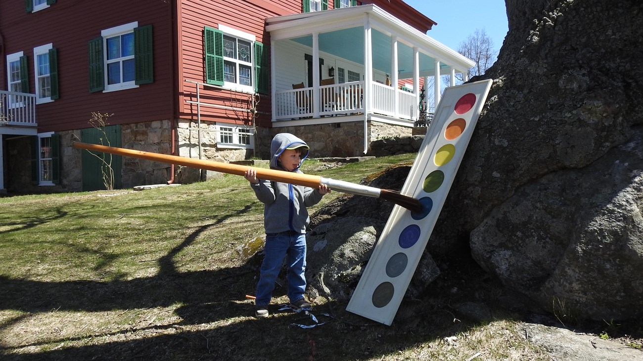 A child lifts an oversize paint brush