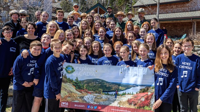 Group of young students pose holding a banner of Acadia National Park. 