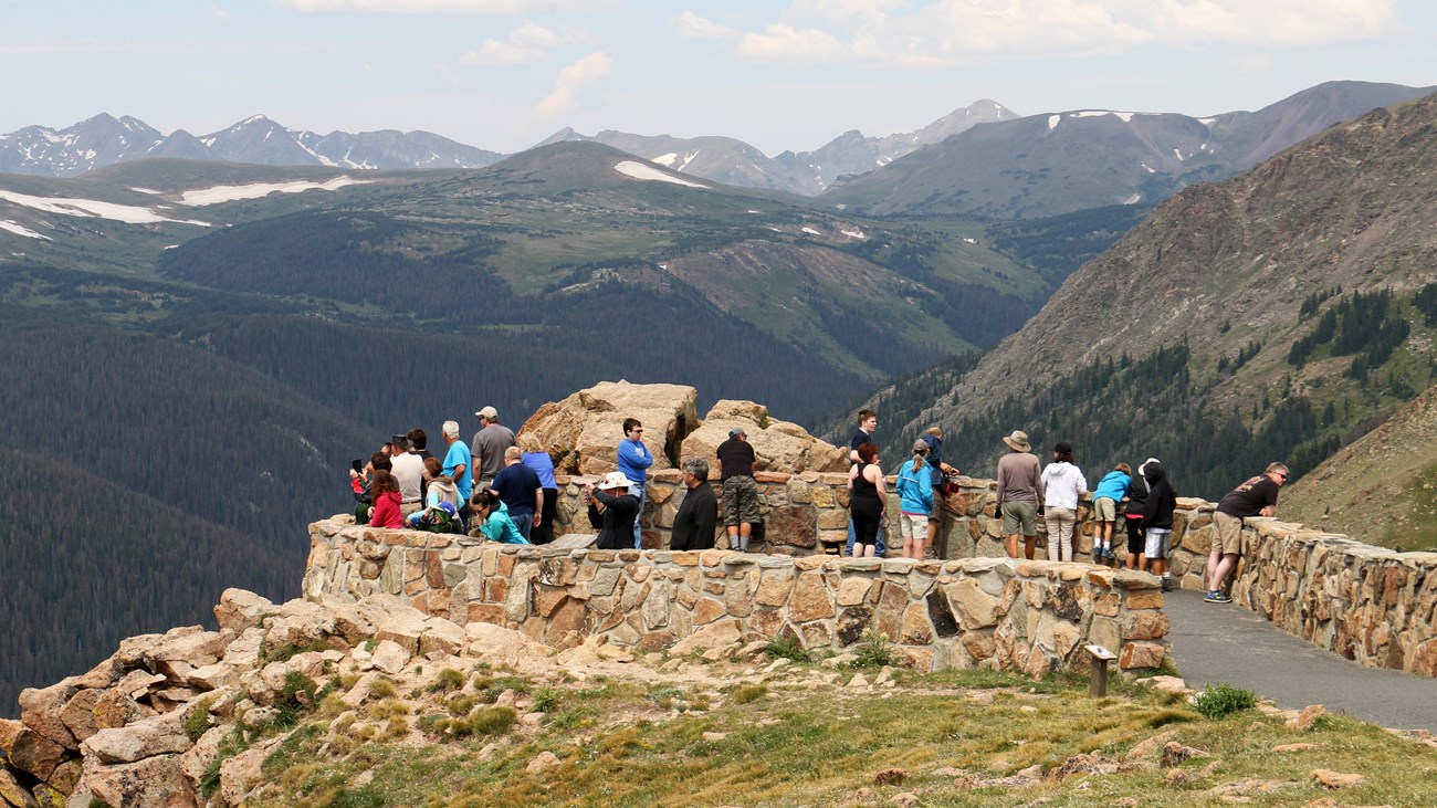 A group of people standing at a scenic overlook, admiring the expansive view of the Rocky Mountains