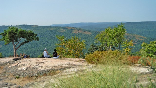 Two people sitting on a rock outcrop overlooking a valley