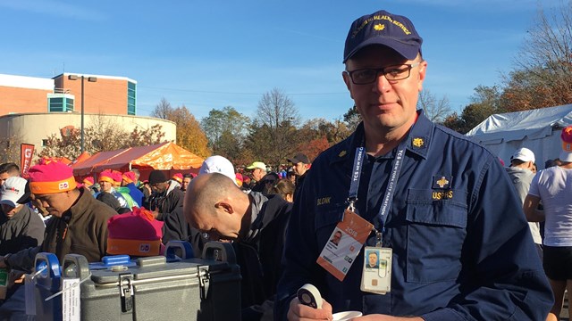 usphs officer stands in a blue uniform next to a table at an outdoor event