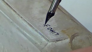 Close-up of a historic glass bottle with a label being applied with a fountain pen and archival ink