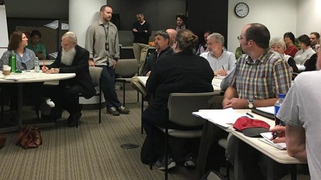 A man stands talking in front of a group.