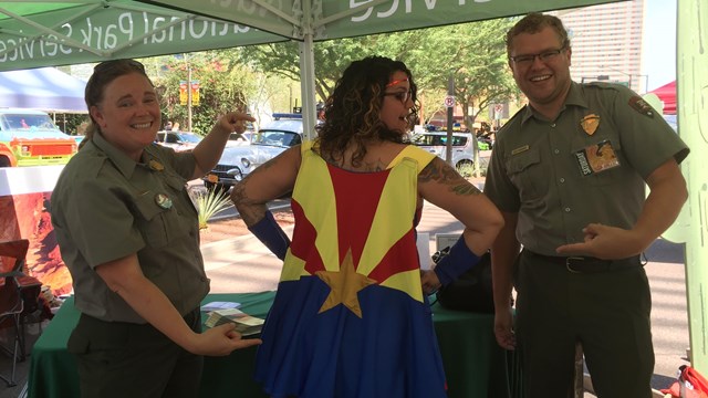 Two rangers stand on either side of a woman with an Arizona Flag cape.