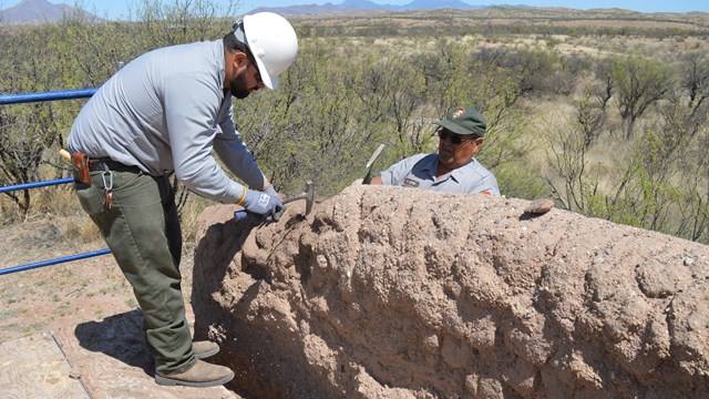 Two men in uniform work on an adobe wall.