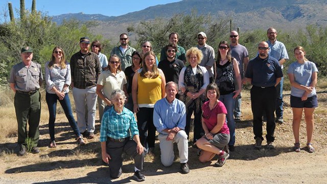 A group of people stand with cactus and a mountain behind them.