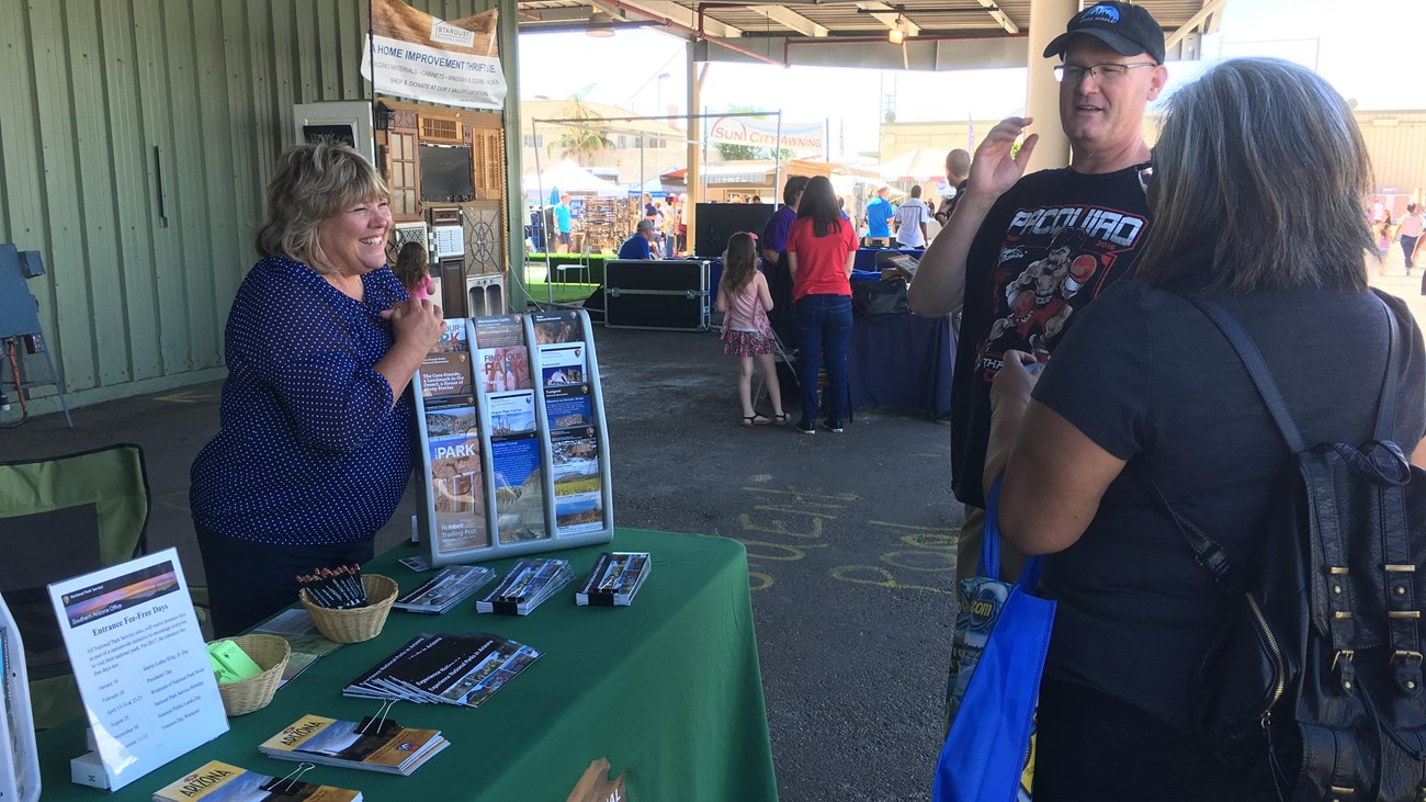 Three people talk at a table with park service brochures and maps.