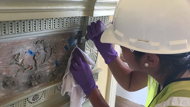 Woman in hardhat and gloves applies epoxy to an ornate mantelpiece decoration