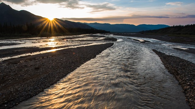 sun behind mountains and a wide, shallow river