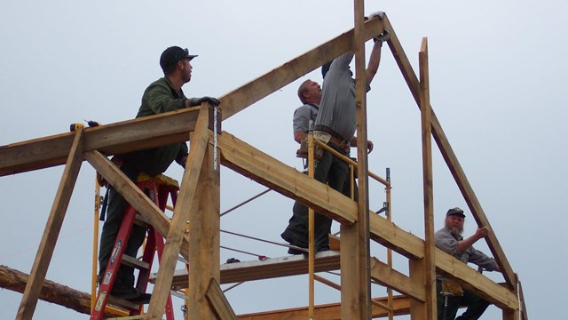 Employees on the timber framing of a barn at Port Oneida Rural Historic District