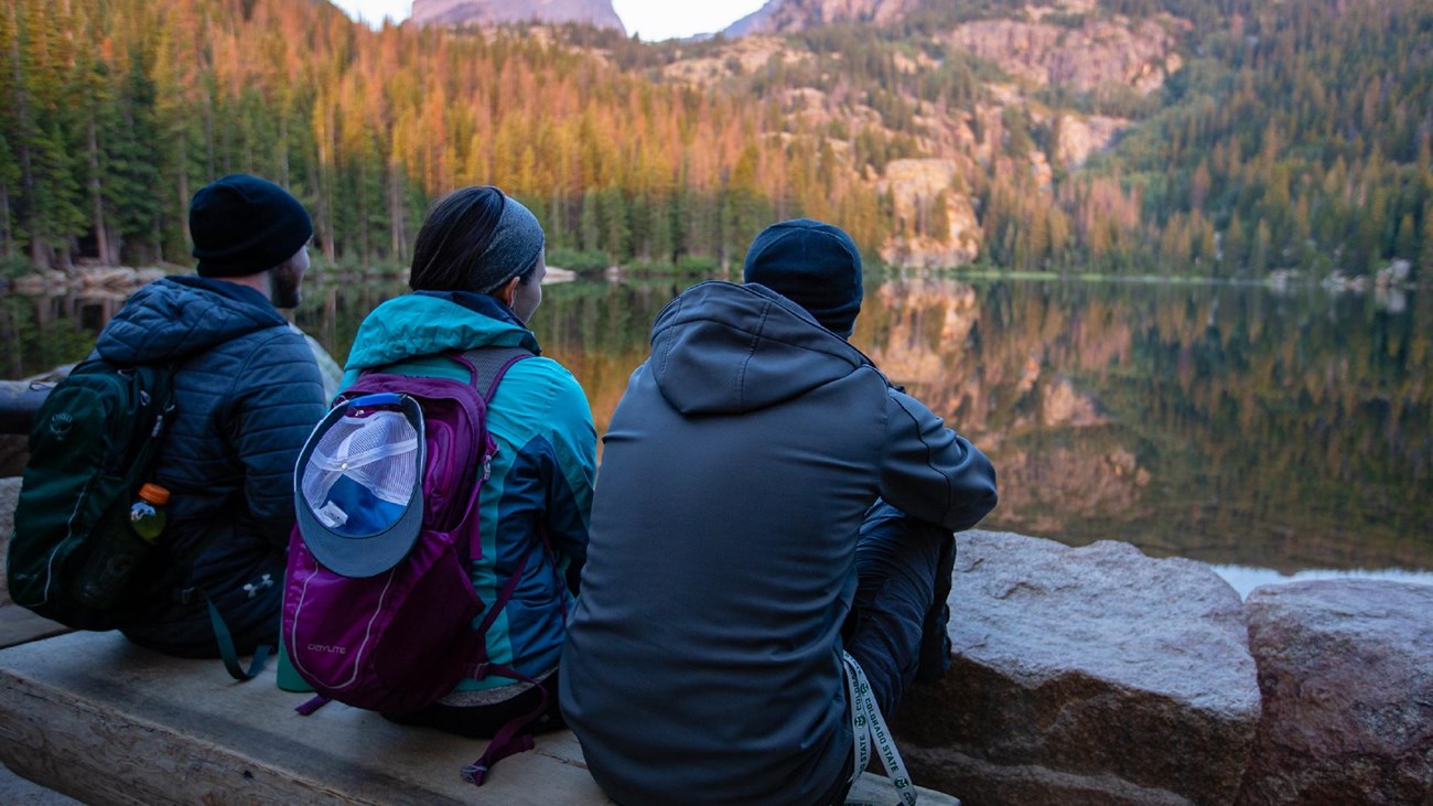 three people sit at the edge of a lake and enjoy the view