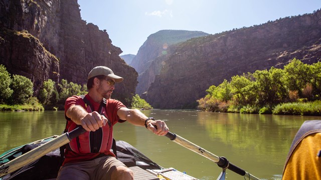 a man rows a boat down a river in a canyon